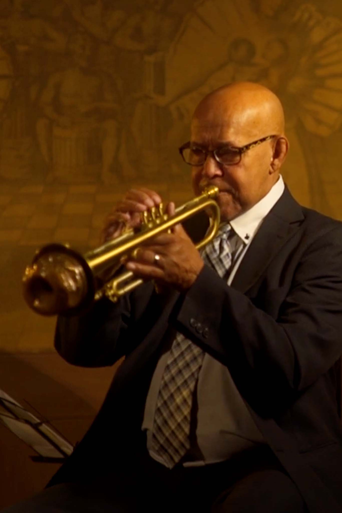 Trumpeter Eddie Henderson sits in a black and white suit, playing his gold trumpet