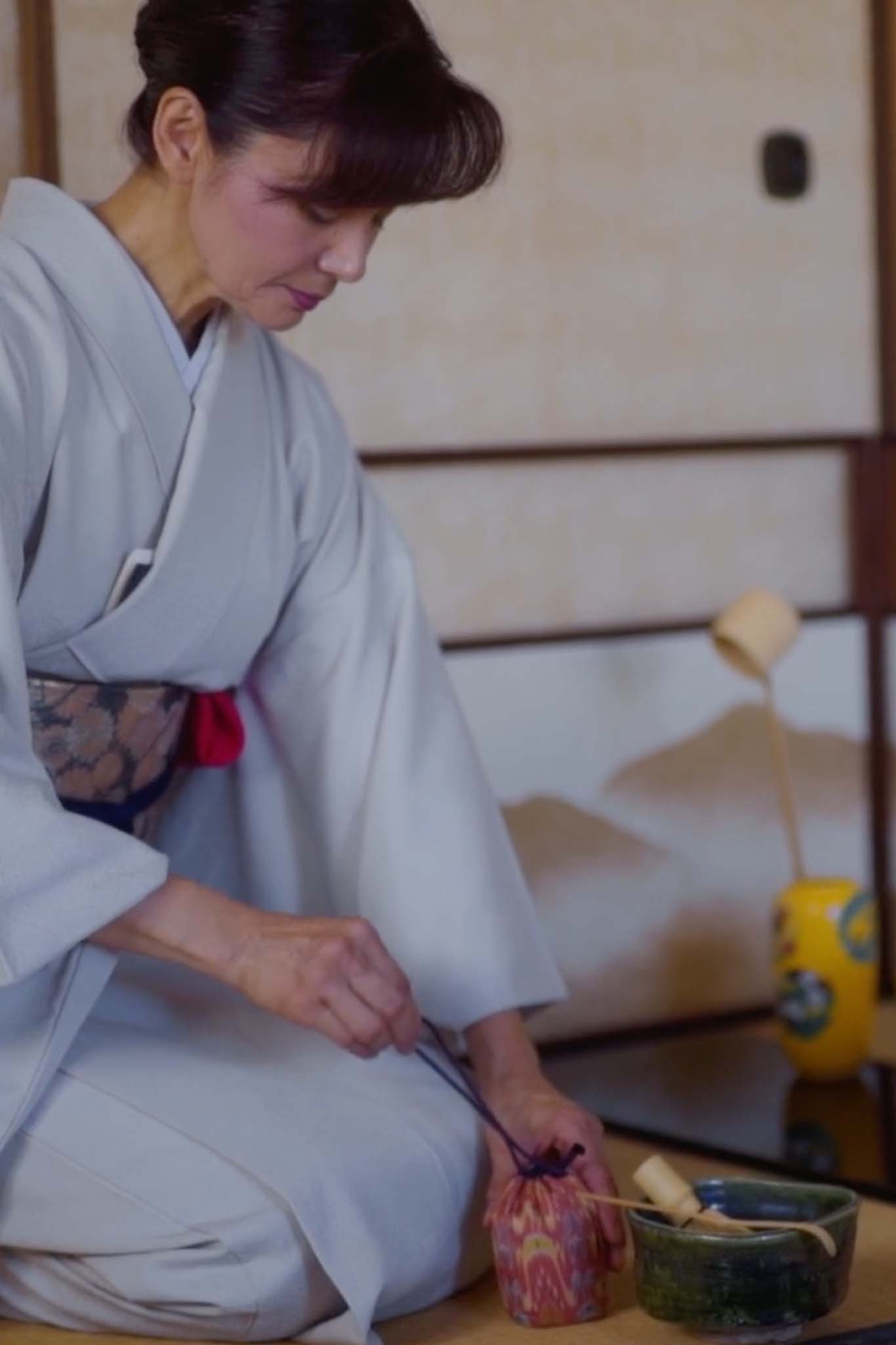 Woman in a kimono carefully prepares tea with ceramic tea cups wrapped in traditional fabric