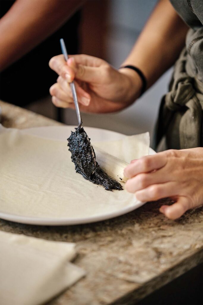 Close-up of hands using a fork to spread a black paste on a flatbread.