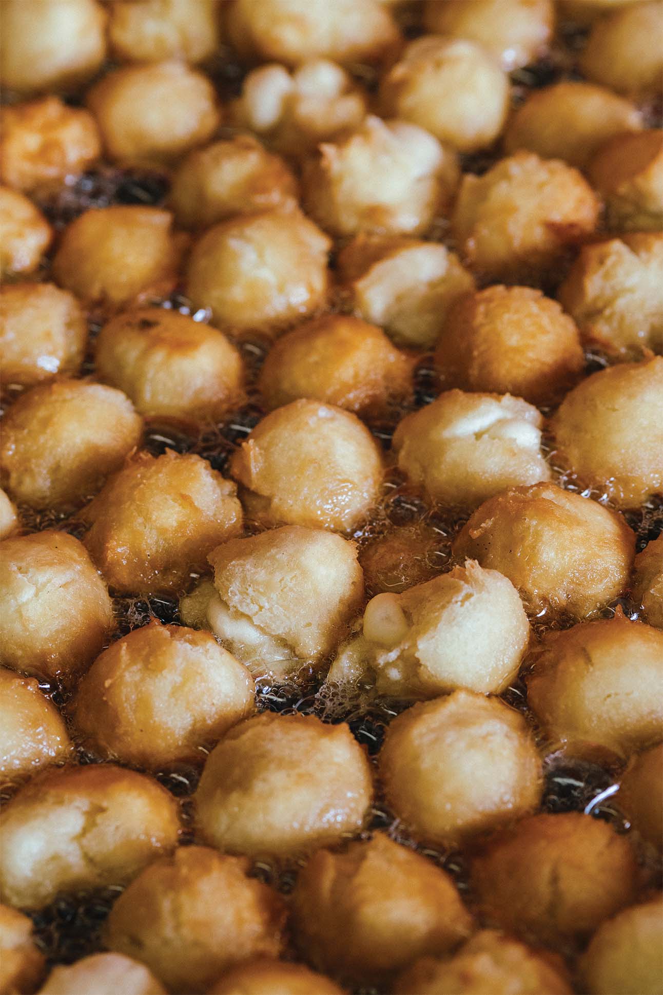 Close up of golden brown dough balls being deep-fried in hot oil.