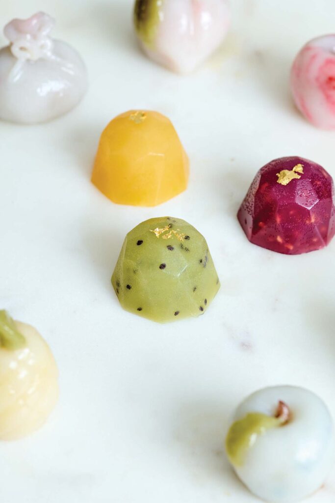 Assorted colorful, shiny chocolates with various artistic designs, arranged on a white surface.