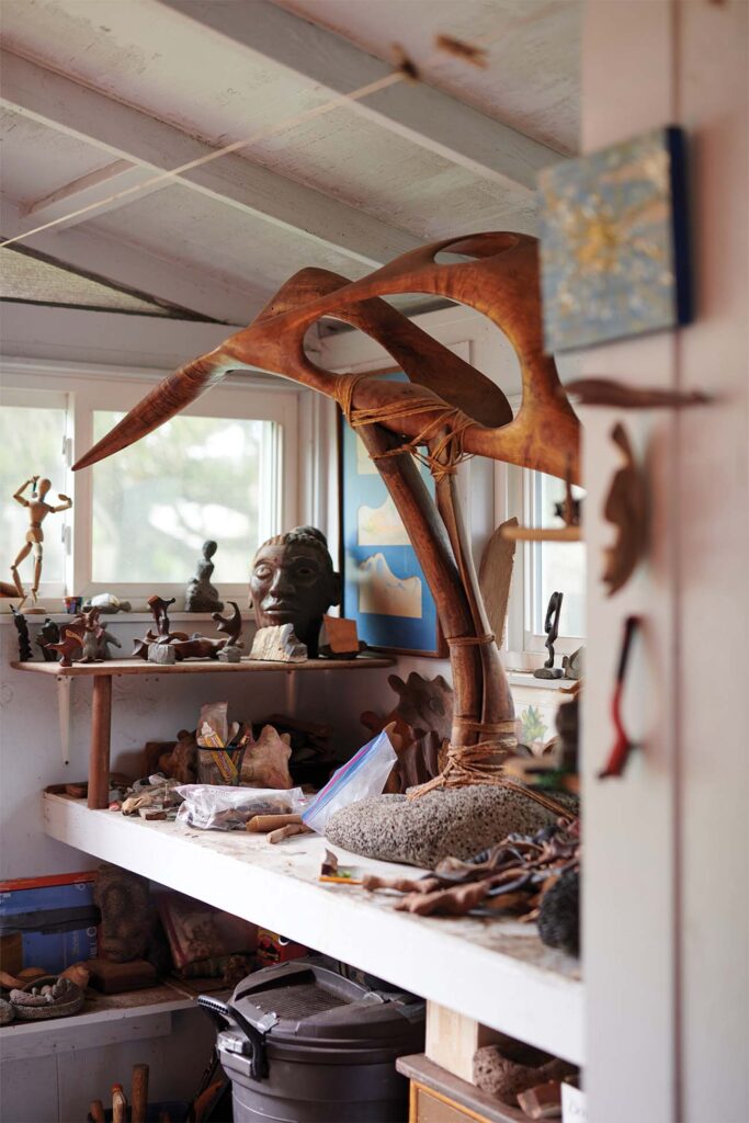 A cluttered artist's studio with a large wooden sculpture prominently displayed in the center